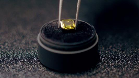 A small yellow diamond crafted from ashes, resting on a black base.