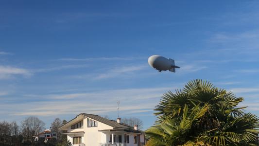 A blimp hovers above houses and a palm tree.