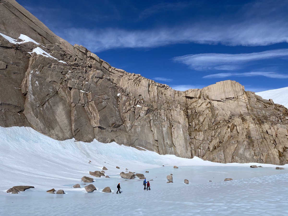 a large cliff with researchers hunting for meteorites in front of it