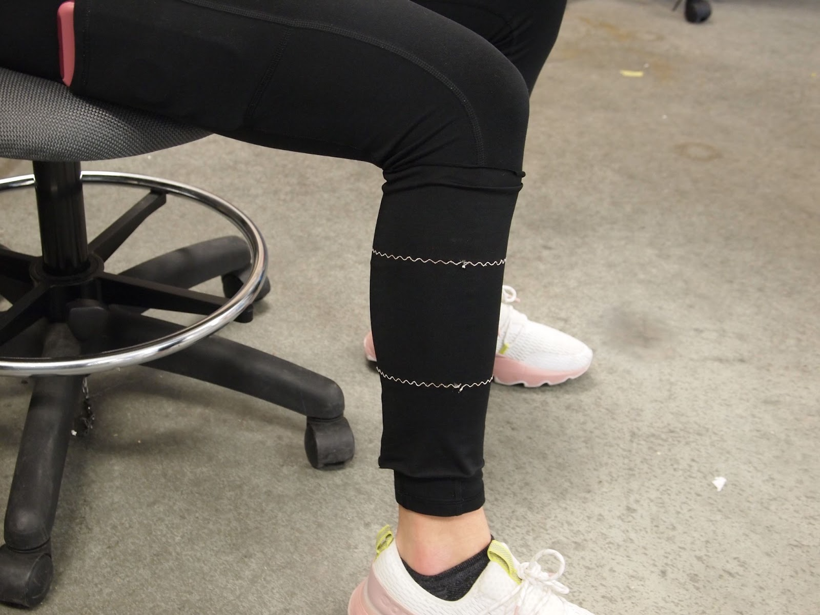 A close up of a leg wearing a black cloth sleeve with two zig-zagged lines of white thread