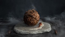 a large meatball on a stone serving platter with a strip of sauce on it