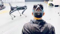 an image of the back of a man's head. he is wearing a headset device. a robot dog is in the background.