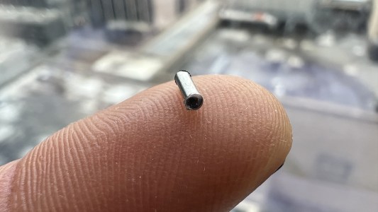 a tiny hollow tube made of shiny silver metal position on the tip of a finger