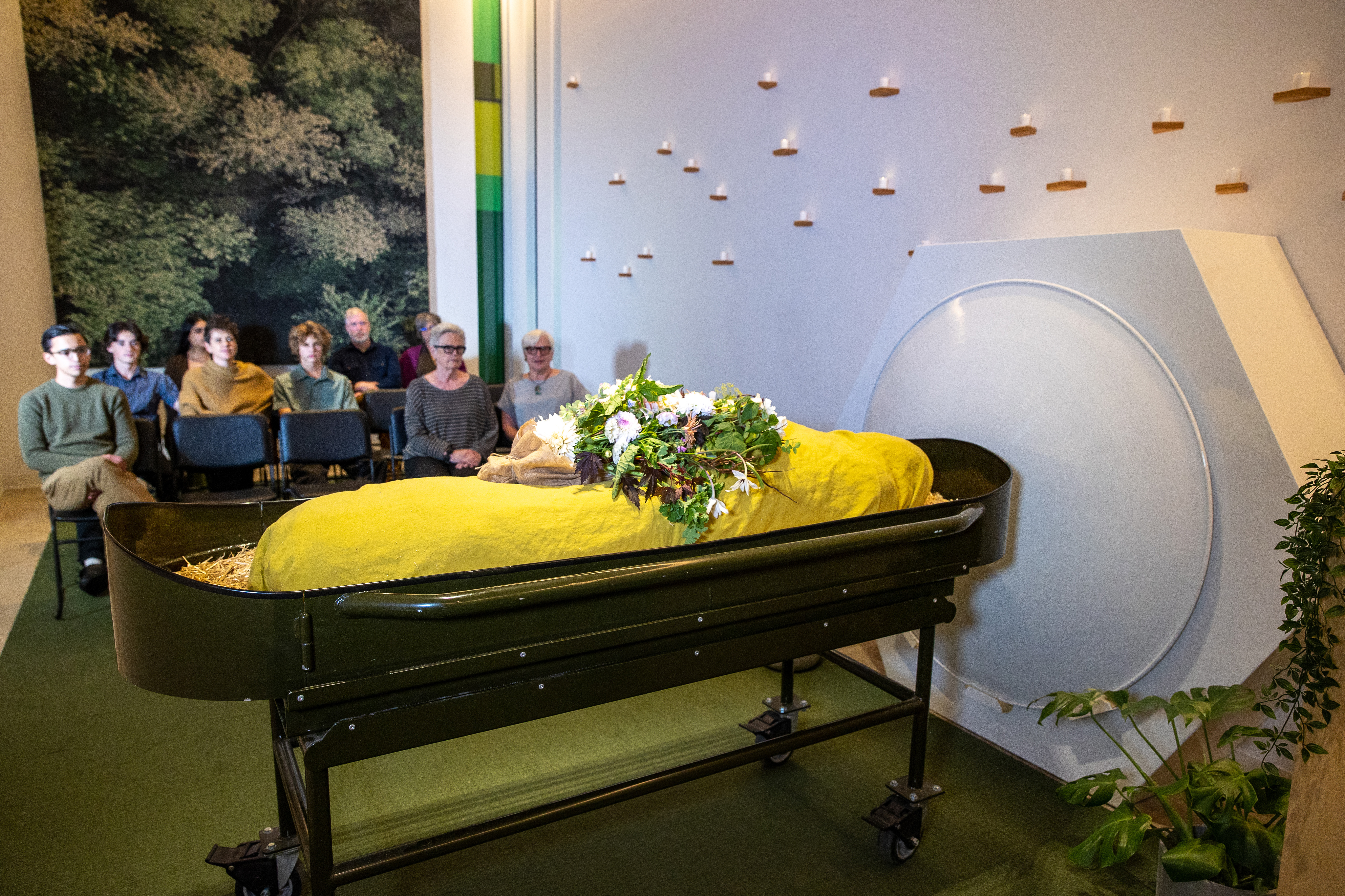 A staged funeral service with a mannequin wrapped in yellow cloth to symbolize the body