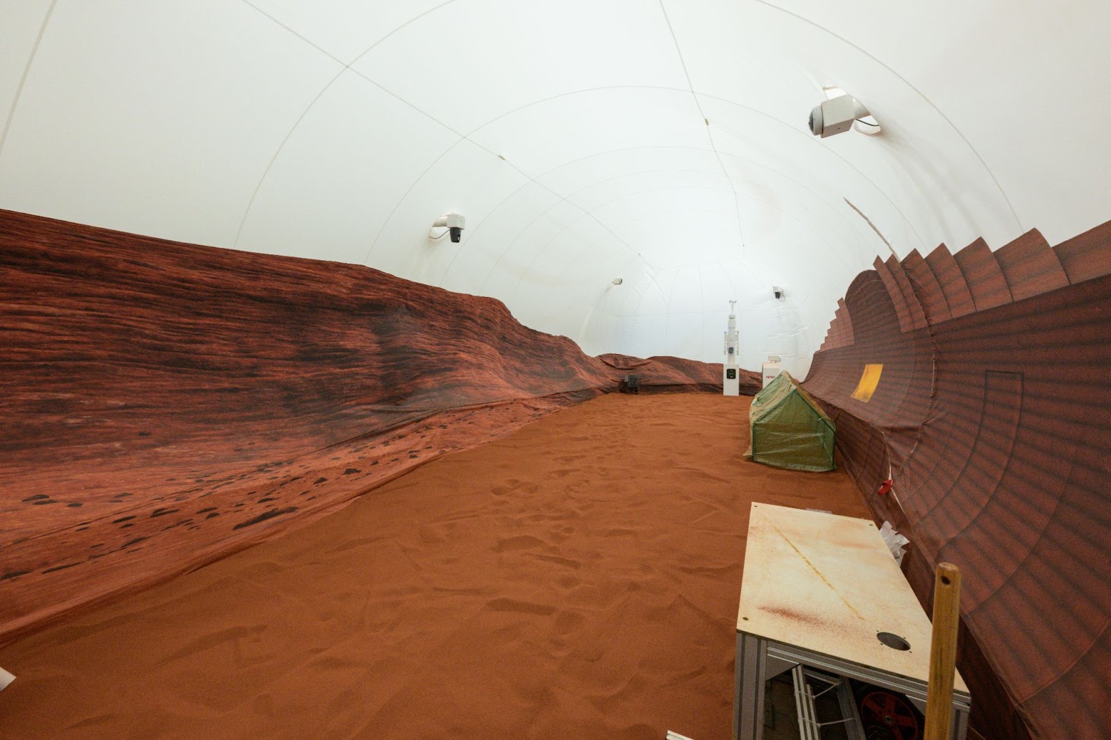 a large room with a floor of red sand and a white fabric roof