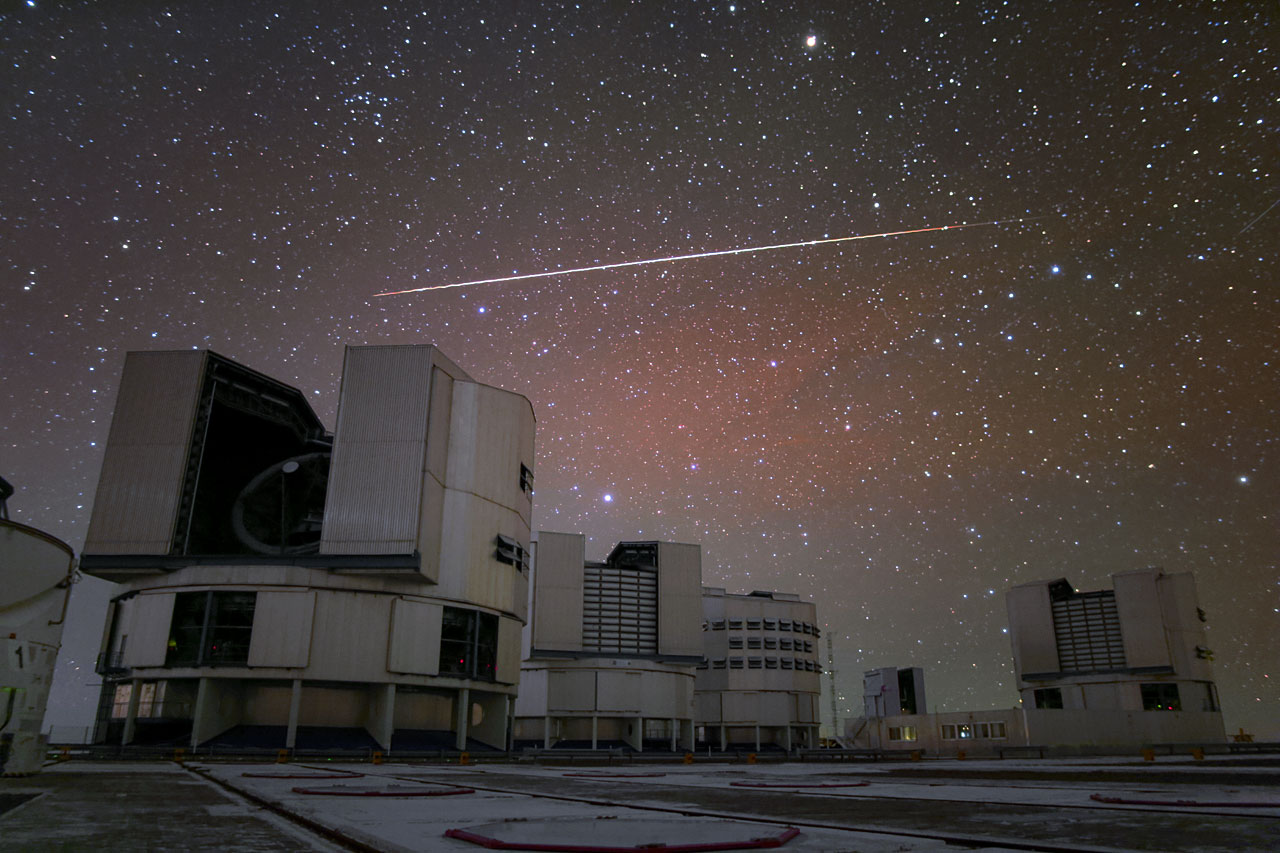 a streak of white is visible in the night sky over a series of buildings