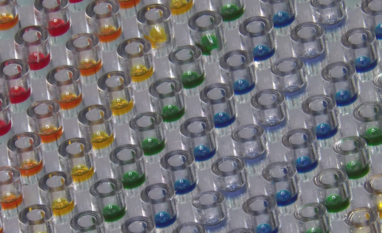 a closeup of dozens of tiny cup-like structures, packed tightly and filled with colorful liquids