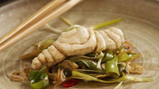 a close up of a piece of white fish on a plate with vegetables and chopsticks