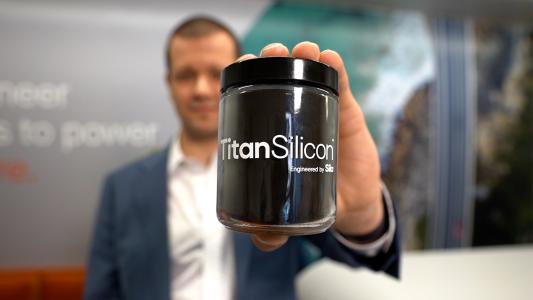 a man holding a container labeled "Titan Silicon" and filled with a black powder
