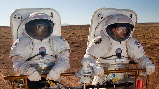 two men in space suits standing in what looks like a dust field