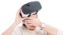 a woman lifting a VR headset off her eyes and holding her temples like she has a headache
