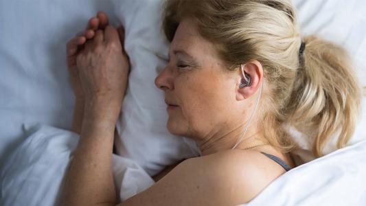 a close up on the side of a woman's face while she sleeps. in her ear is a small device
