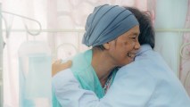 a smiling patient in a headwrap hugging another person