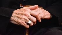 A close-up of an elderly person's hands on a cane.