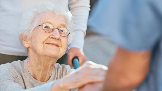 a seated older woman looking up toward a healthcare worker