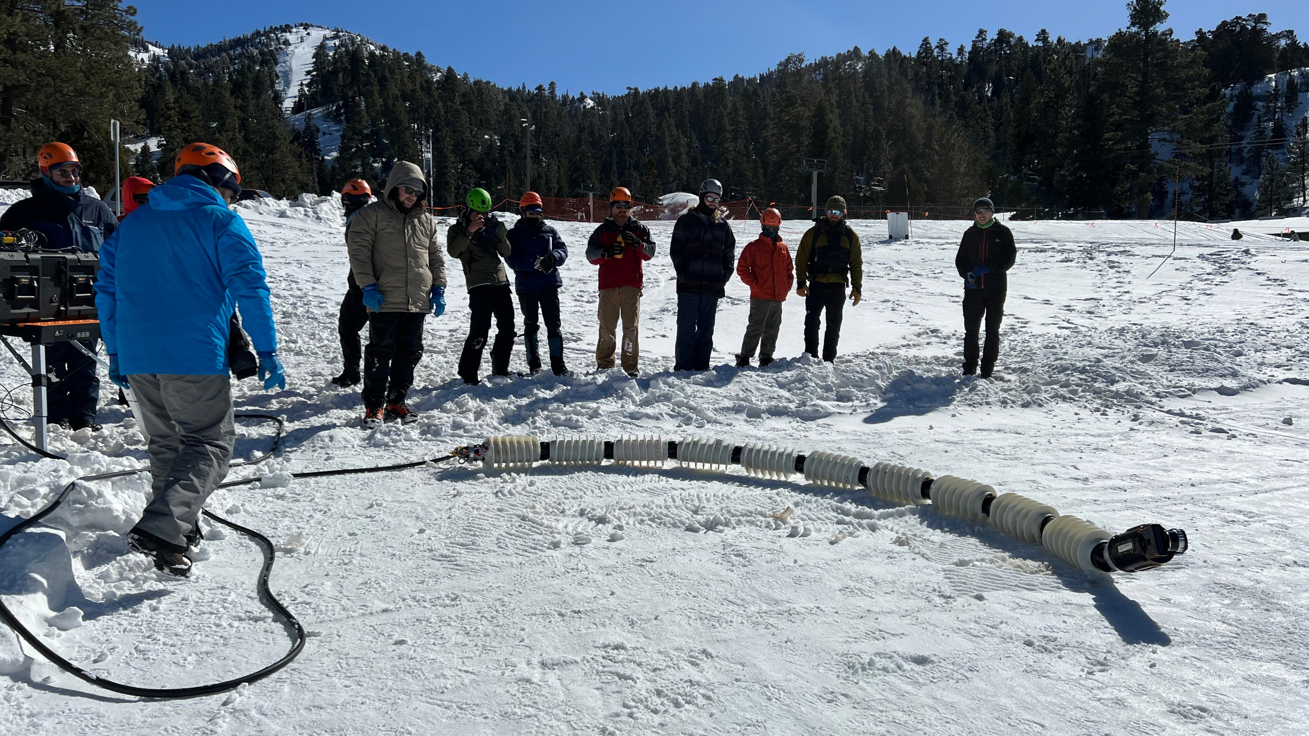 The EELS snake robot on the snowy ground with researchers standing around it