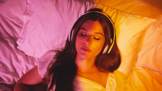 a female-presenting person wearing headphones while lying in bed. her eyes are closed.