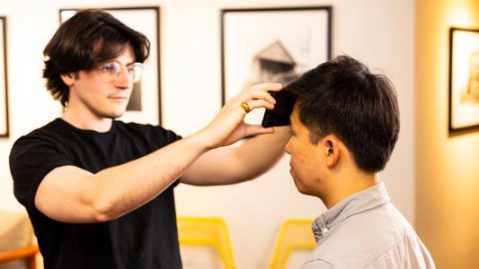 a man holds a smartphone screen to another man's forehead to measure his temperature