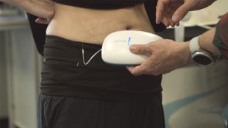 a closeup of a person's waist with a thin tube connecting it to a device held in another person's hand