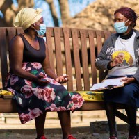 Two women sitting on a bench wearing face masks.