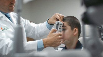 A doctor is examining a boy's eye for signs of butterfly skin disease, considering potential treatment options such as topical gene therapy.