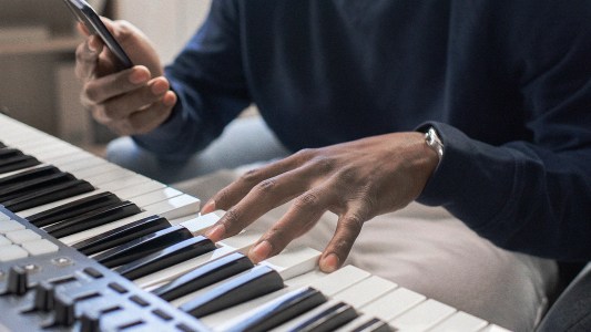 A man engaging in neurogenesis while playing a piano and using a cell phone.