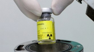 A person is injecting a yellow radiopharmaceutical liquid into a container.