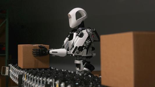 A humanoid robot is moving boxes in a warehouse.