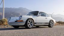 A white porsche 911 parked in front of wind turbines.