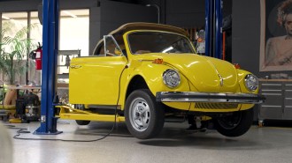 A yellow volkswagen beetle is being worked on in a garage.