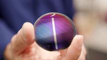 A person is holding up a small circular solar cell made from lunar regolith.