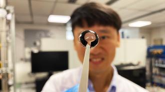 A man in a lab holding a smart contact lens in front of the camera