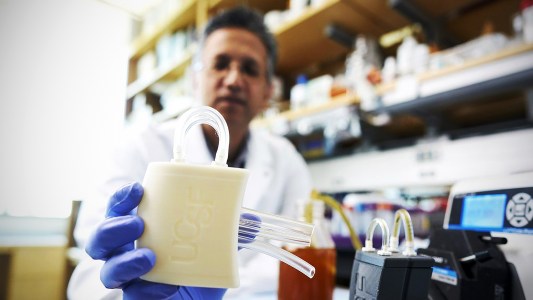 A man in a lab holding a beige, rectangular container with tubes extending from it