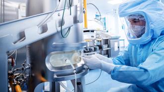 A person in a protective suit is working on a machine related to Covid-19 vaccines.