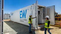 Two workers standing next to a large container containing iron-flow batteries for renewable energy storage.