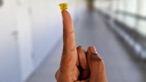 A person's finger is holding up a small yellow suction cup