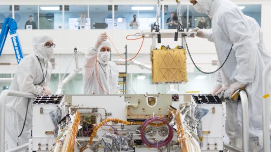 NASA engineers in a lab lowering MOXIE into a Mars rover