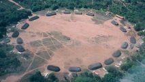 An aerial view of a circle of huts in the forest.