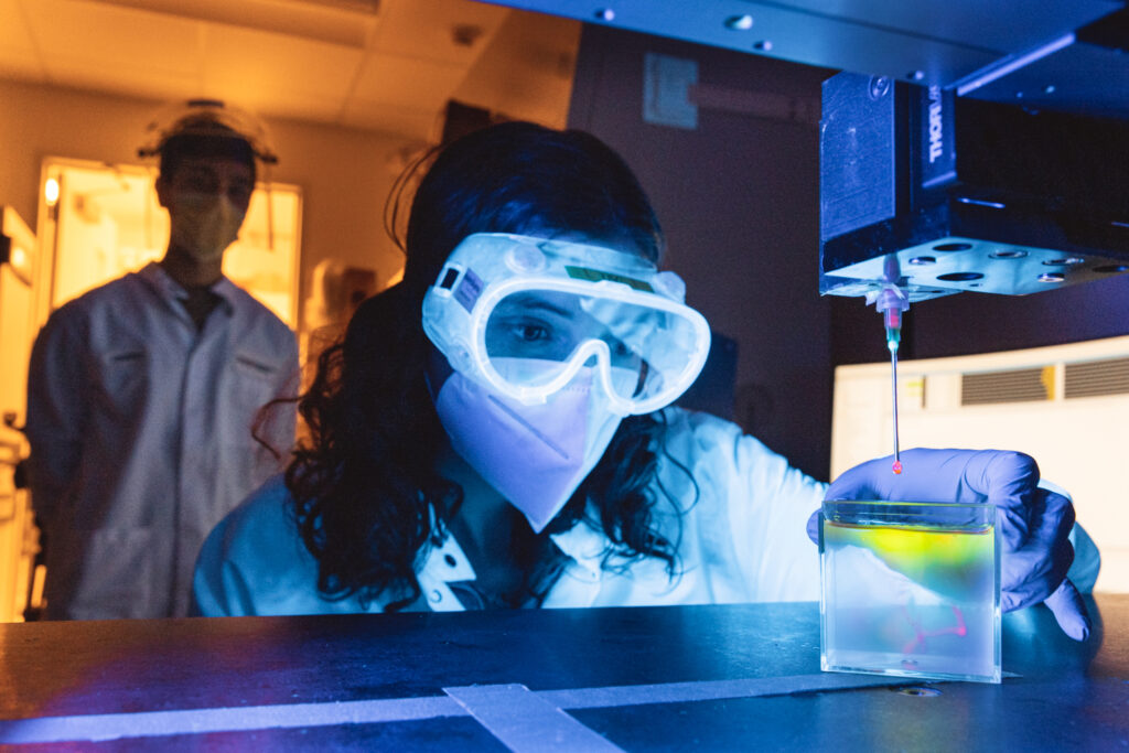 A woman in a lab coat and goggles is 3D bioprinting something in her lab