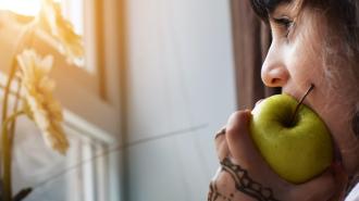 A girl is eating an apple in front of a window.