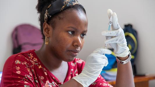 A woman preparing to administer a malaria vaccine with a syringe.