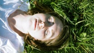 A woman laying in the grass with her eyes closed.