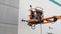 the robot painter at the end of a lift, painting a gray building white