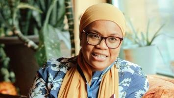 A woman wearing a hijab sitting on an orange couch.