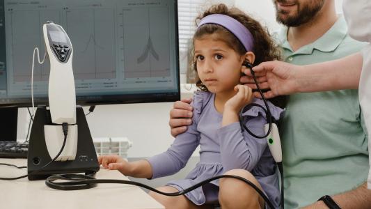 a young girl is sitting on a man's lap while a doctor tests her hearing