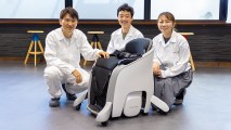Three people posing for a photo with Honda's hands-free wheelchair