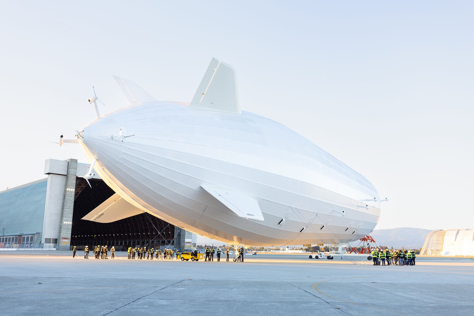 A large white airship outside of a hangar