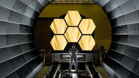 A man standing in a tunnel with a large number of hexagons, mesmerized by the intricate patterns formed by the JWST.