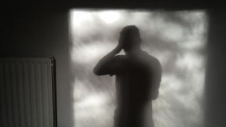 A shadowy figure standing in front of a radiator, symbolic of the silent struggles often associated with mental health.