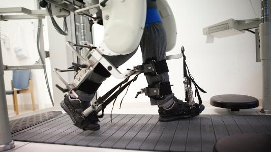 a close-up of a person's legs as they walk on a treadmill, with an exoskeleton providing support